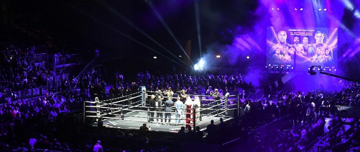 Rudolf Weber-Arena Oberhausen bei der Crossover Fight Night 2023: Ring in der Hallenmitte, Publikum auf den Raengen, Videowand mit dem Eventplakat.